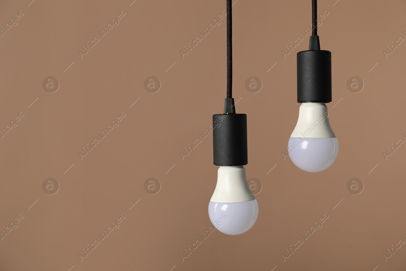 Photo of Light bulbs hanging on cords against beige background, space for text