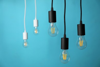 Photo of Light bulbs hanging on cords against blue background, selective focus