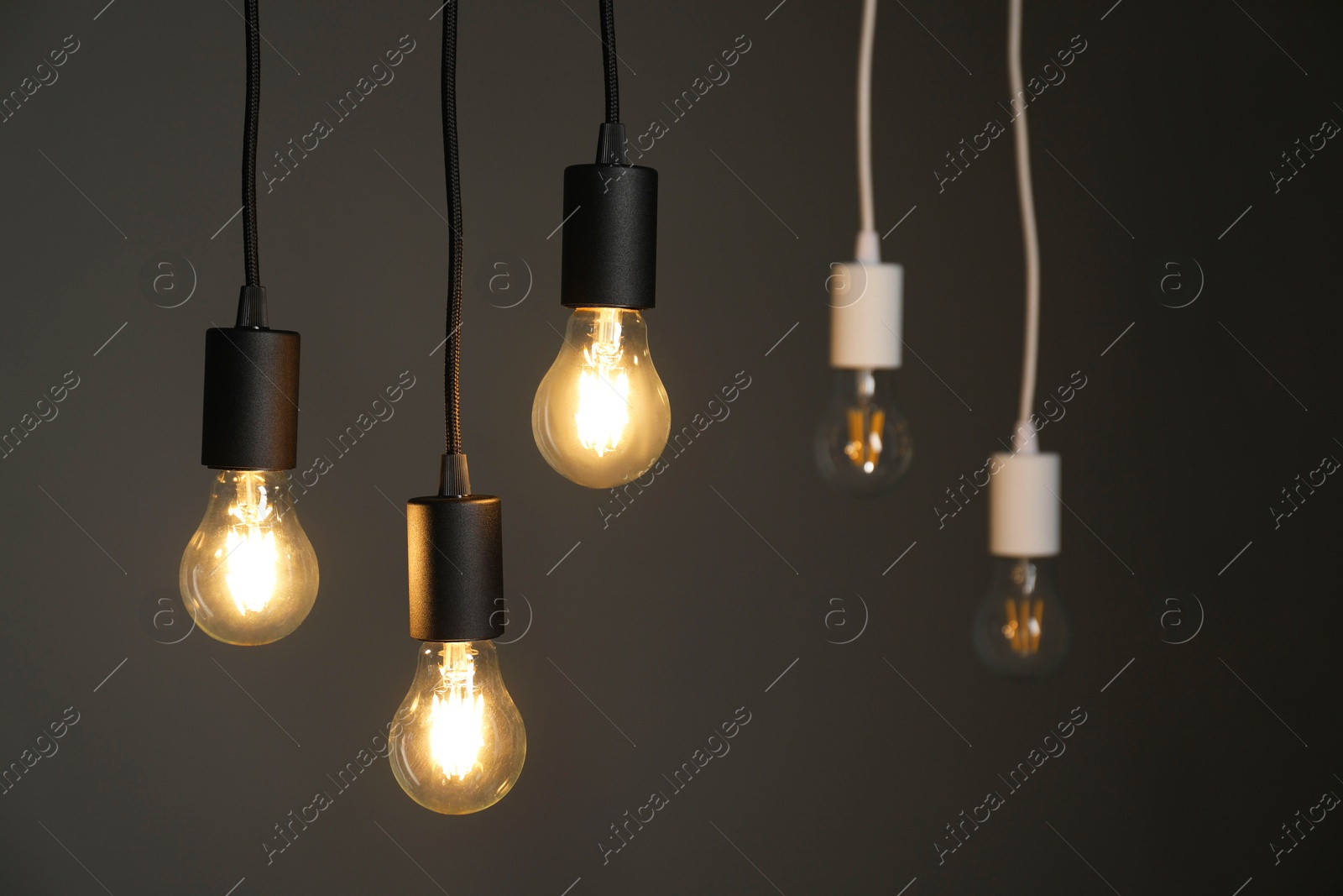 Photo of Light bulbs hanging on cords against grey background, selective focus