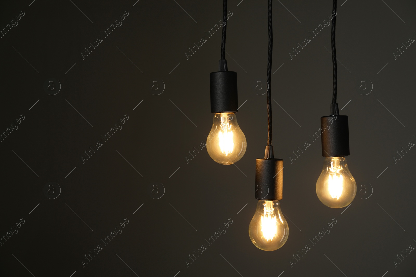 Photo of Light bulbs hanging on cords against grey background, space for text