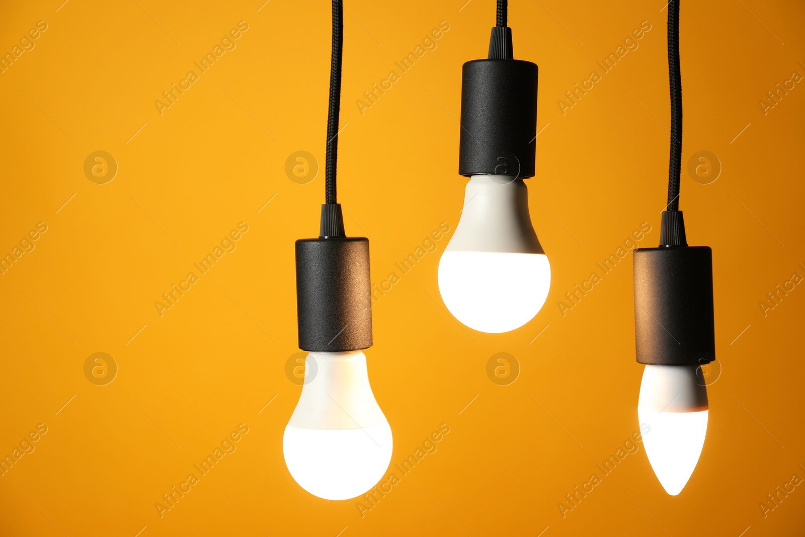 Photo of Light bulbs hanging on cords against orange background, space for text