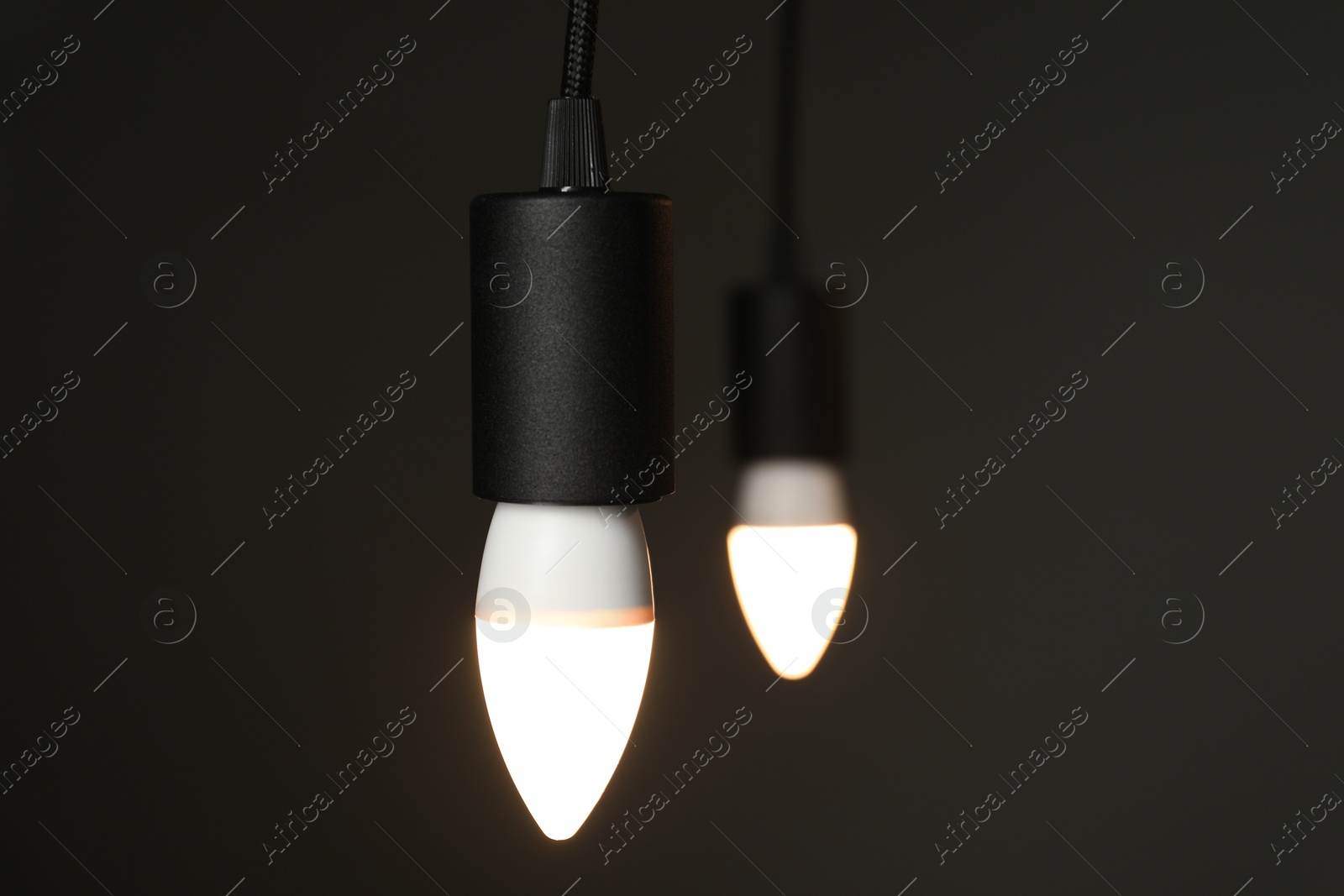 Photo of Light bulbs hanging on cords against grey background, selective focus. Space for text