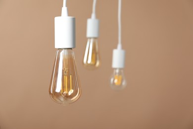 Photo of Light bulbs hanging on cords against beige background, selective focus. Space for text