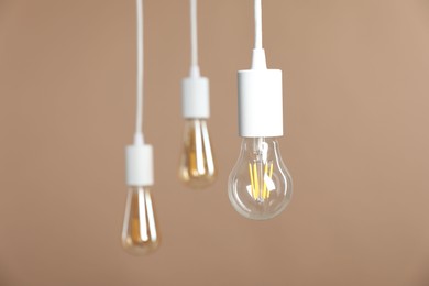 Photo of Light bulbs hanging on cords against beige background, selective focus. Space for text