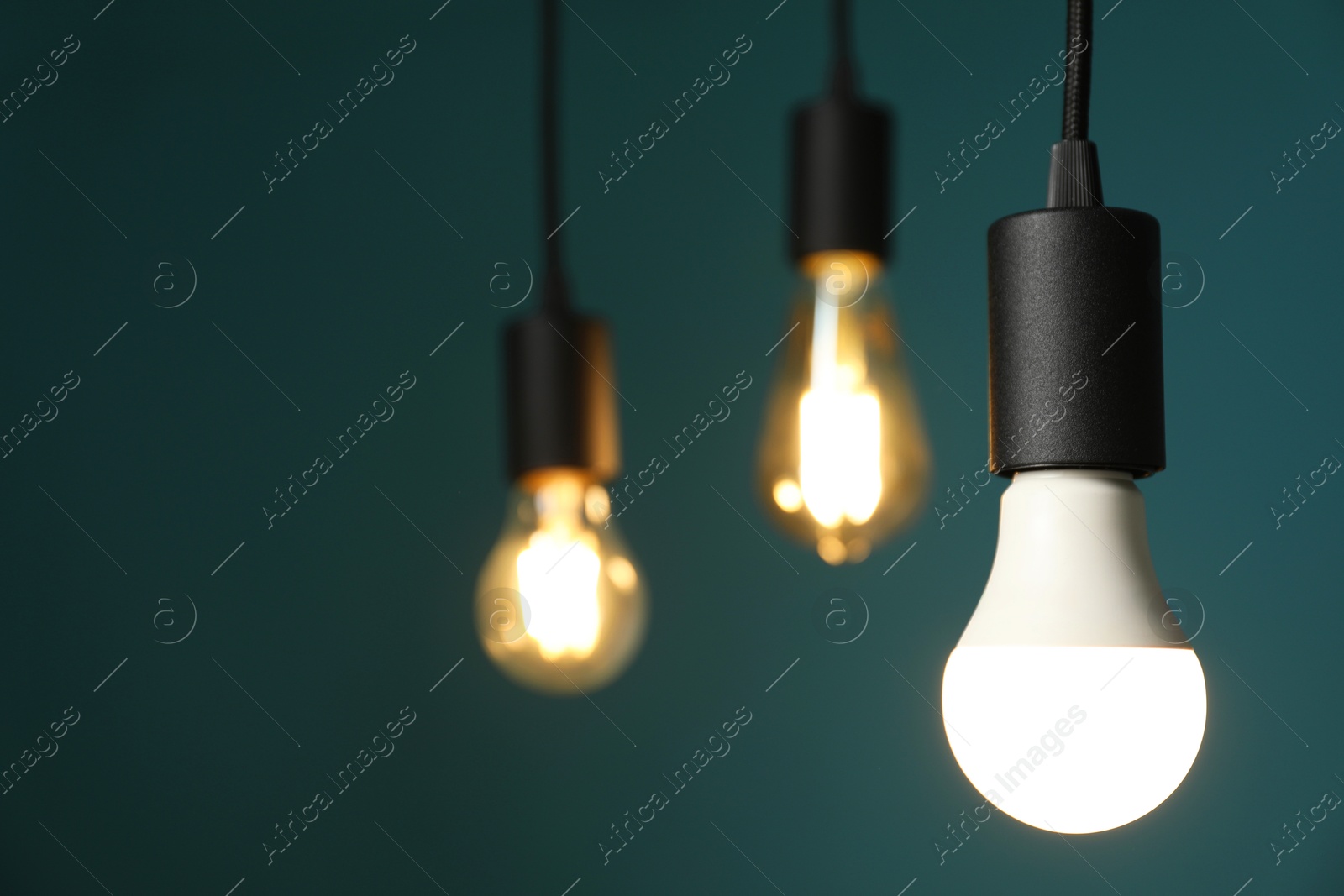 Photo of Light bulbs hanging on cords against teal background, selective focus. Space for text