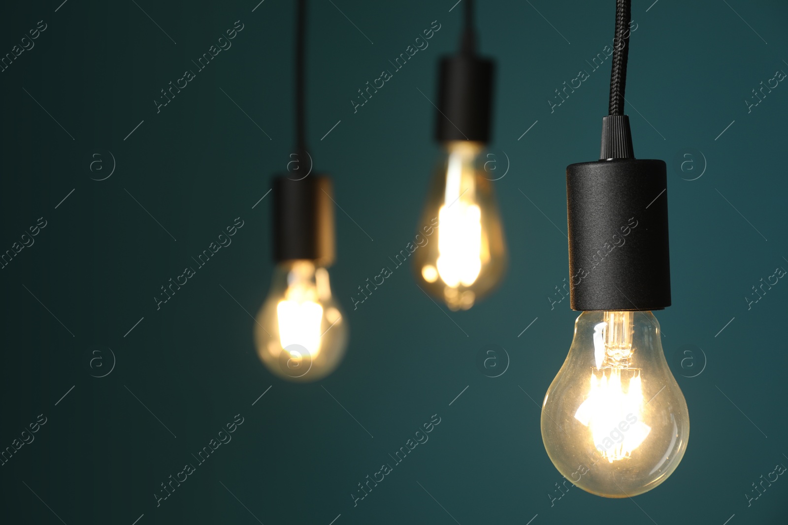 Photo of Light bulbs hanging on cords against teal background, selective focus. Space for text