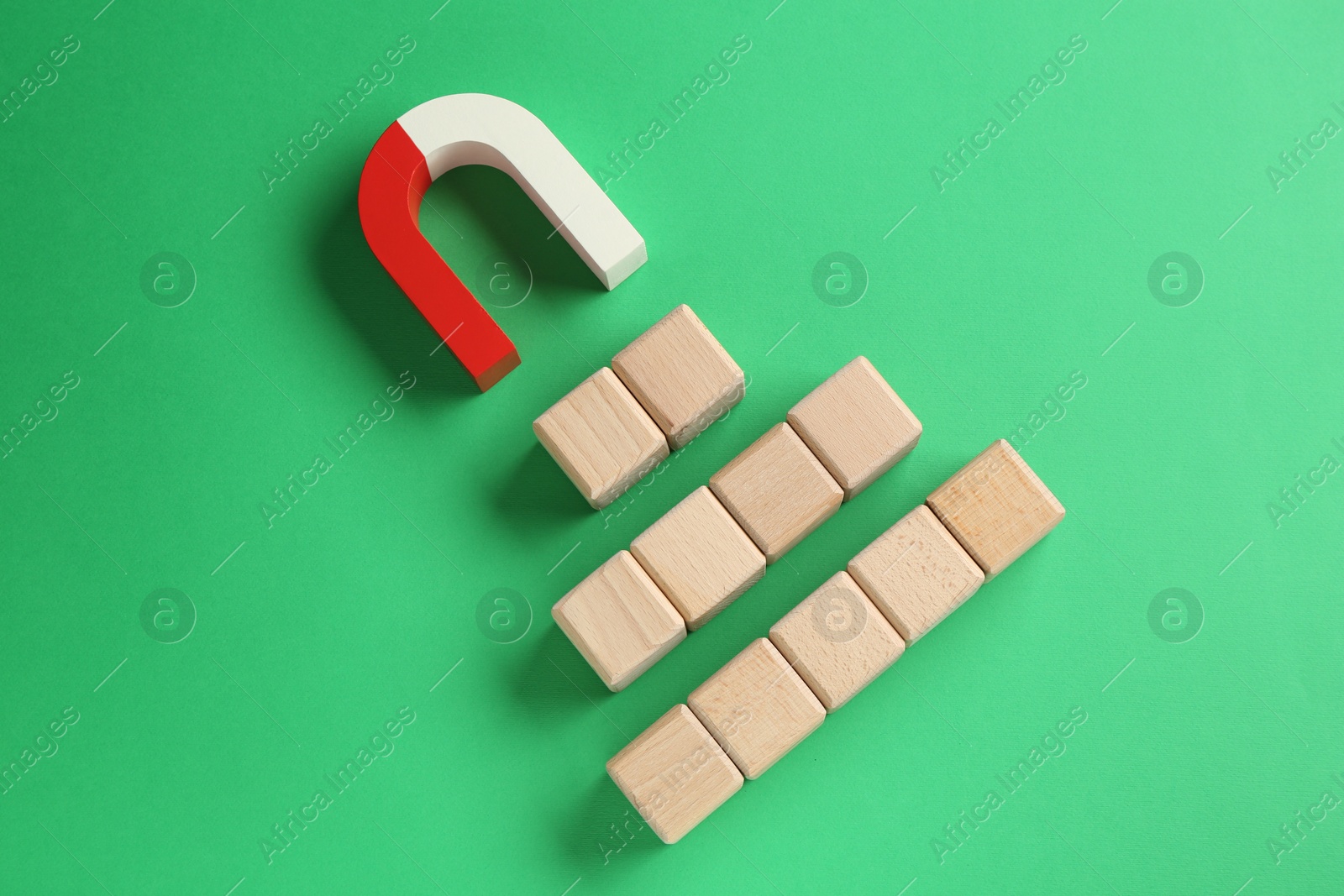 Photo of Magnet attracting wooden cubes on green background, flat lay