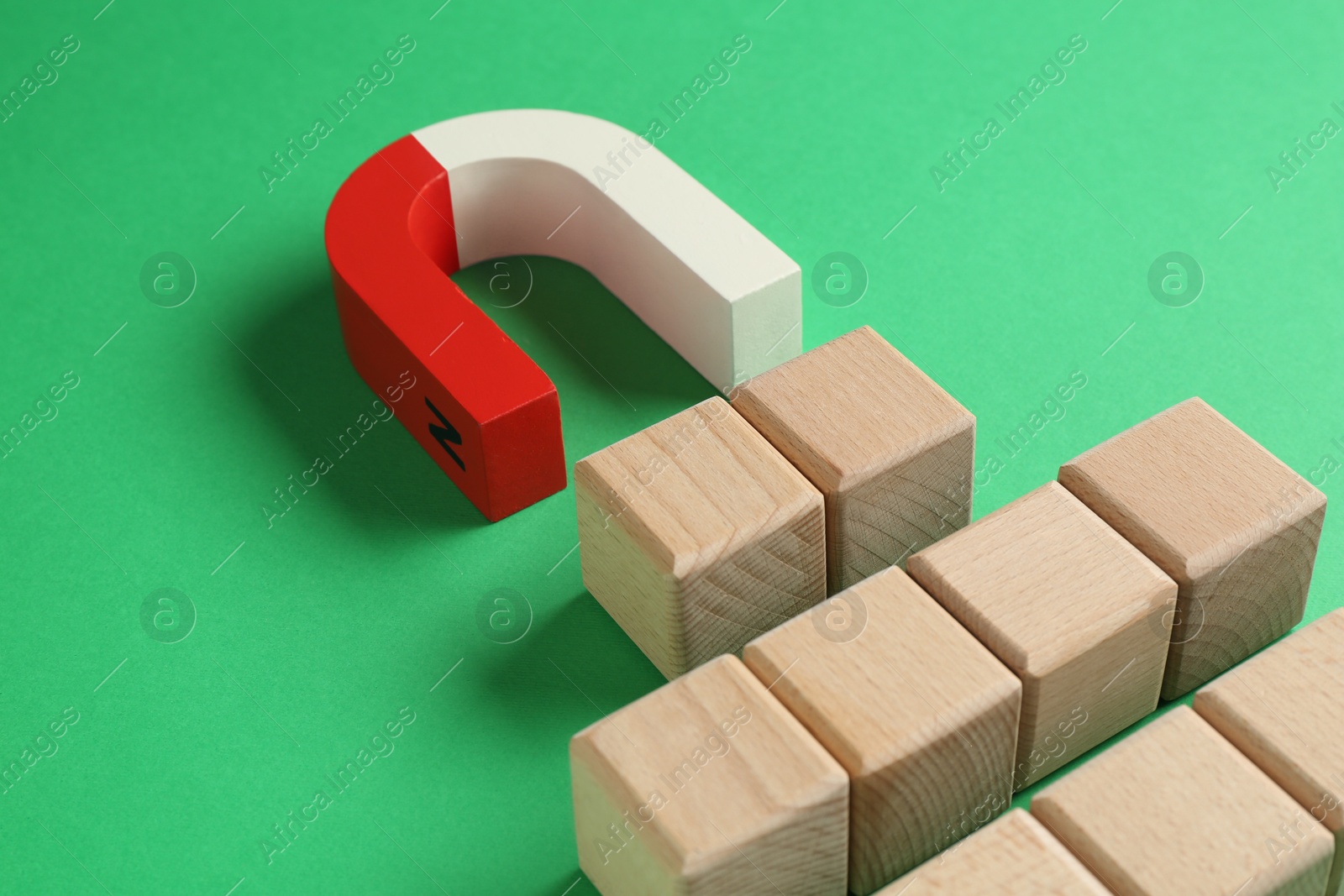 Photo of Magnet attracting wooden cubes on green background, closeup