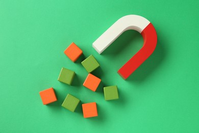 Photo of Magnet attracting colorful cubes on green background, flat lay