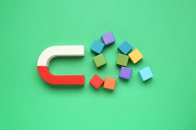 Photo of Magnet attracting colorful cubes on green background, flat lay