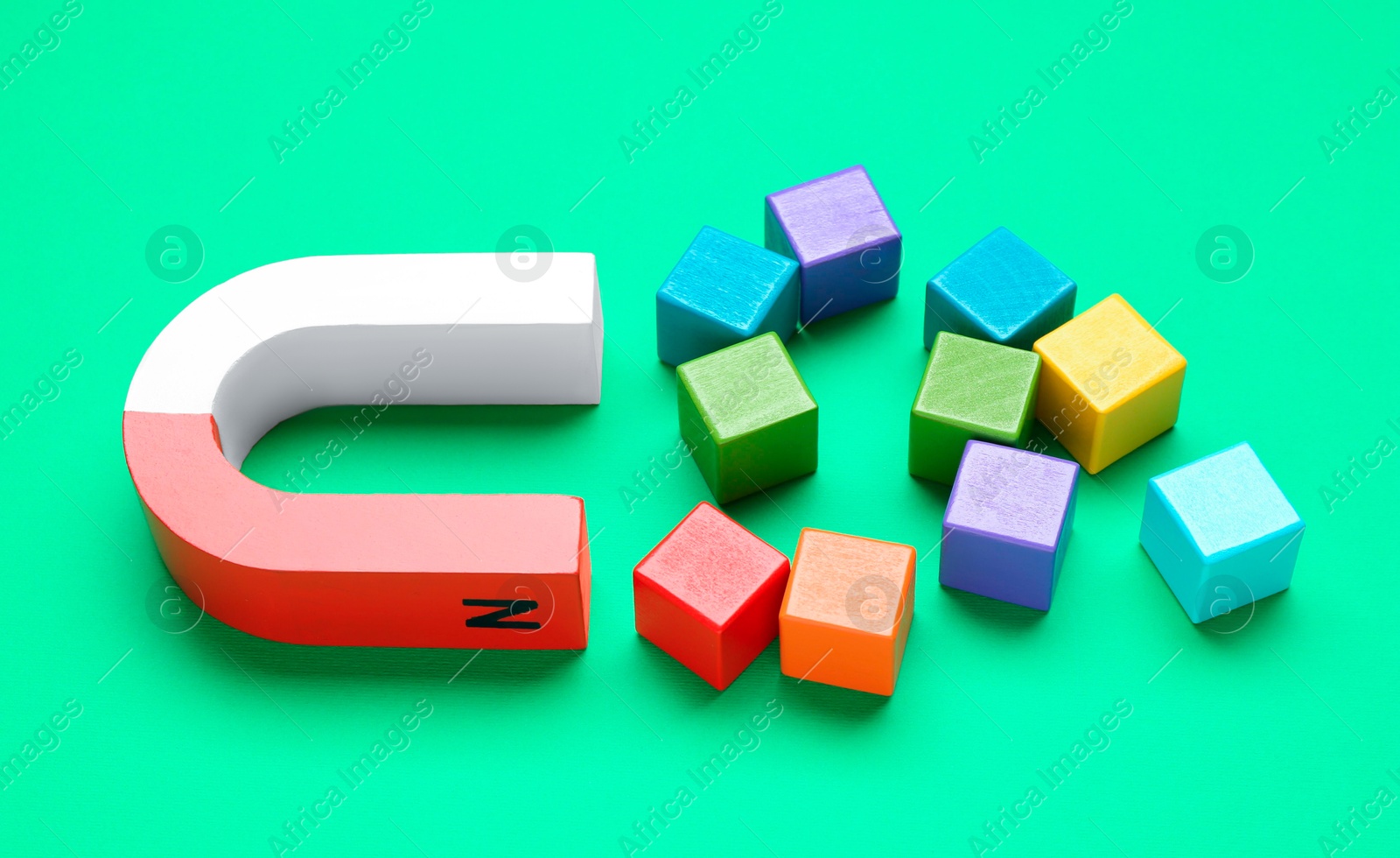 Photo of Magnet attracting colorful cubes on green background