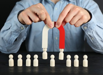 Photo of Man with magnet attracting human figures at black wooden table, closeup