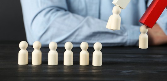 Photo of Man with magnet attracting human figures at black wooden table, closeup