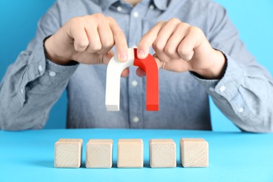 Photo of Man with magnet attracting wooden cubes on light blue background, closeup