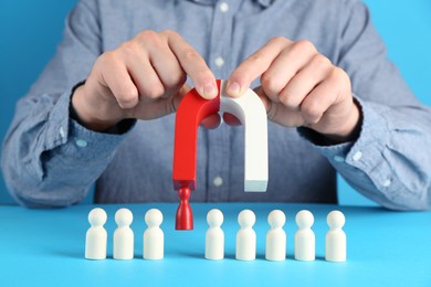 Photo of Man with magnet attracting red piece among wooden ones on light blue background, closeup