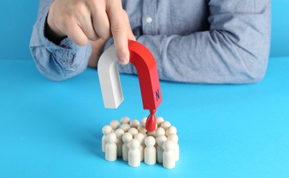 Photo of Man with magnet attracting red piece among wooden ones on light blue background, closeup