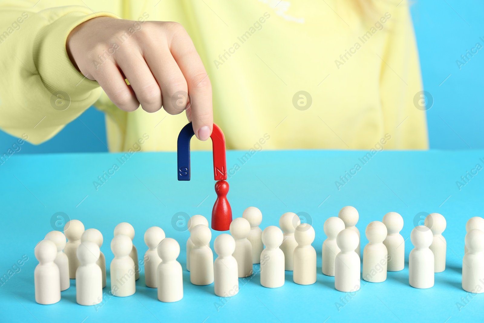 Photo of Woman with magnet attracting red piece among wooden ones on light blue background, closeup