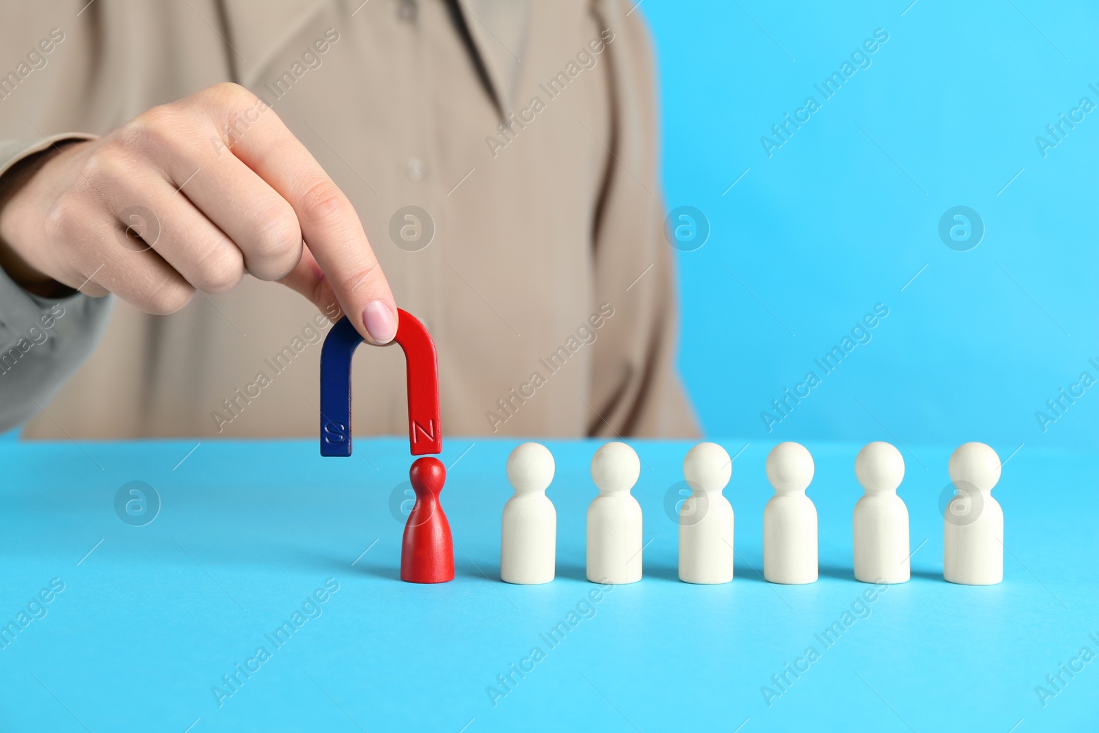 Photo of Woman with magnet attracting red piece among wooden ones on light blue background, closeup