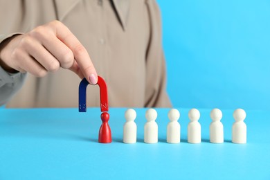 Photo of Woman with magnet attracting red piece among wooden ones on light blue background, closeup