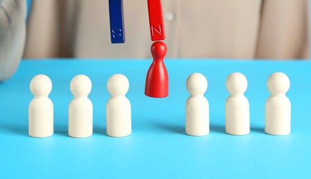 Photo of Attracting red piece among wooden ones with magnet on light blue background, closeup