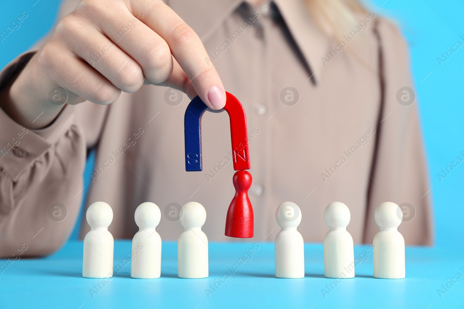 Photo of Woman with magnet attracting red piece among wooden ones on light blue background, closeup