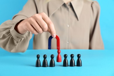 Photo of Woman with magnet attracting red piece among black ones on light blue background, closeup