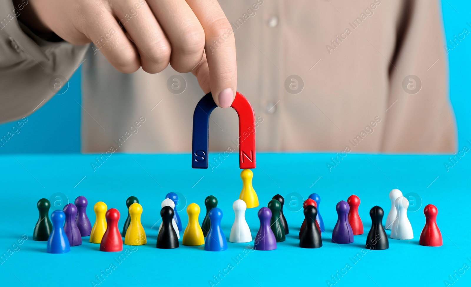 Photo of Woman with magnet attracting yellow piece among colorful ones on light blue background, closeup