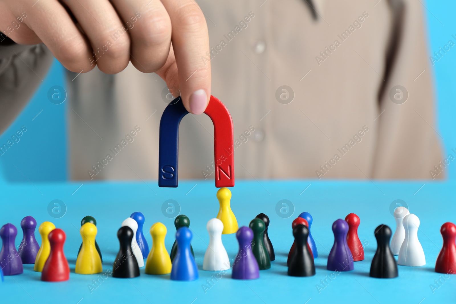 Photo of Woman with magnet attracting yellow piece among colorful ones on light blue background, closeup