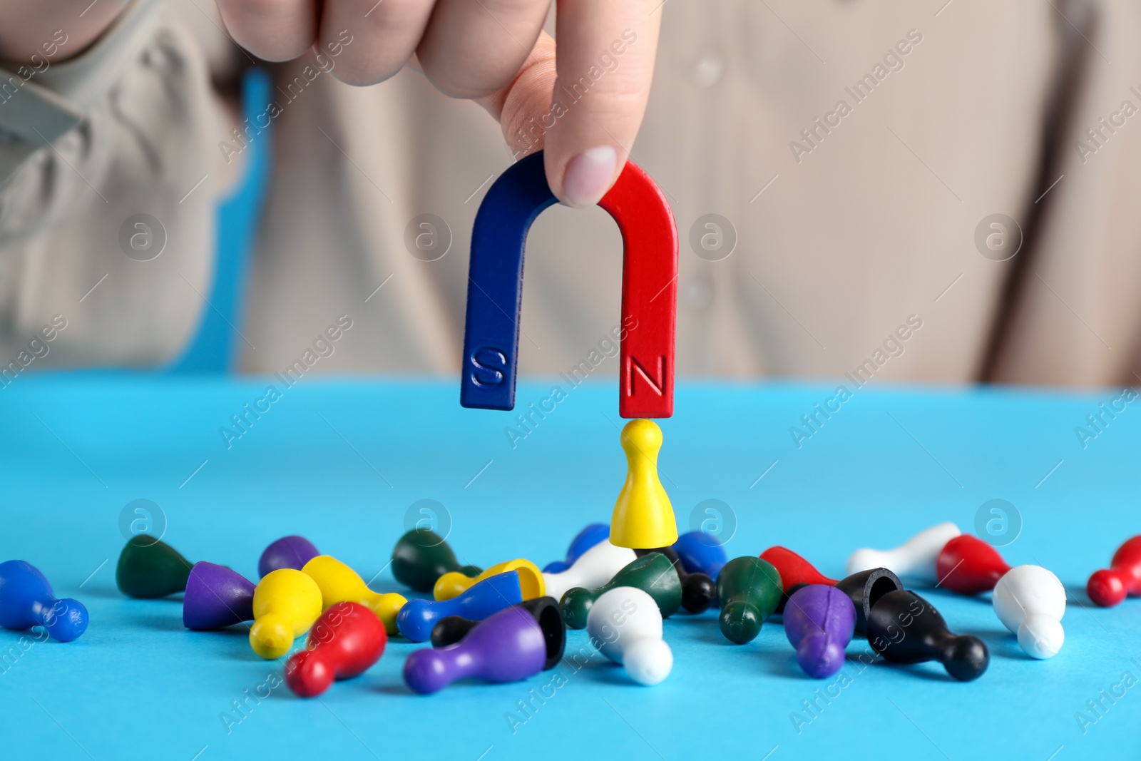 Photo of Woman with magnet attracting yellow piece among colorful ones on light blue background, closeup