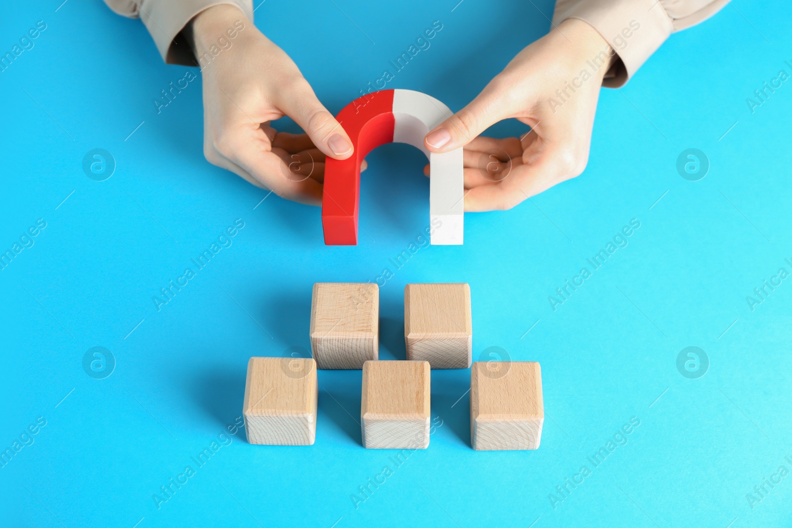 Photo of Woman with magnet attracting wooden cubes on light blue background, closeup