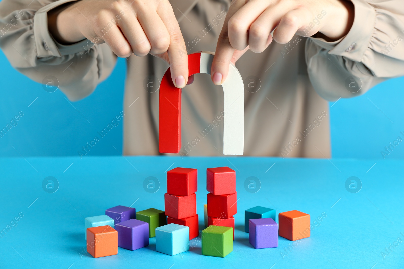 Photo of Woman with magnet attracting colorful cubes on light blue background, closeup