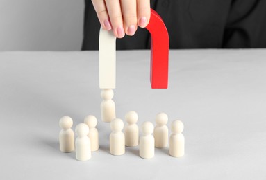 Photo of Woman with magnet attracting piece among wooden ones at white table, closeup