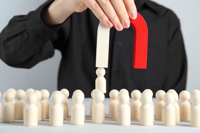 Woman with magnet attracting piece among wooden ones at white table, closeup