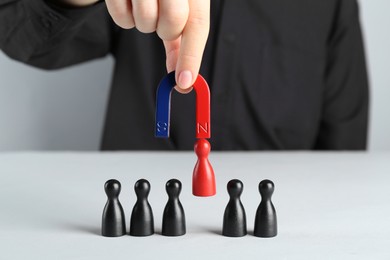 Photo of Woman with magnet attracting red piece among black ones at white table, closeup