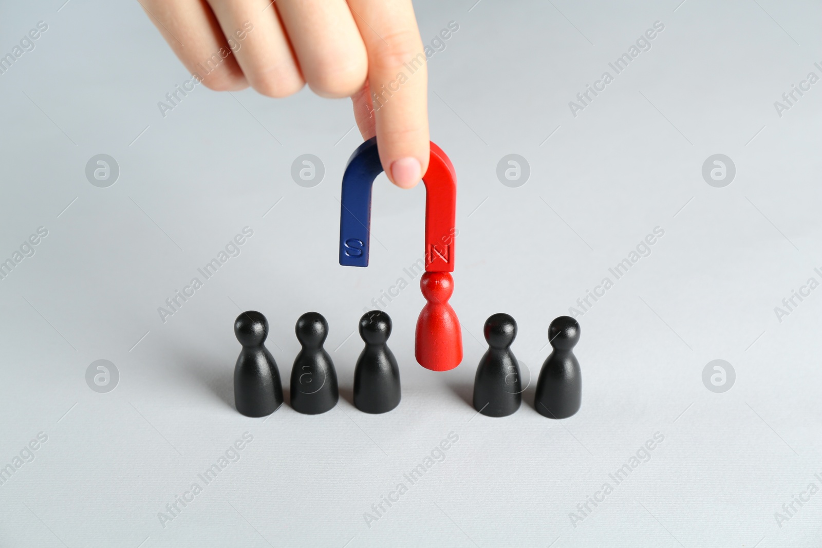 Photo of Woman with magnet attracting red piece among black ones at white table, closeup