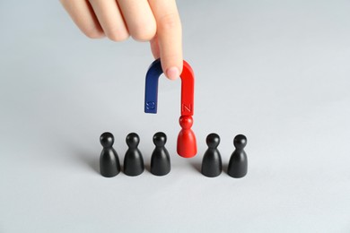 Photo of Woman with magnet attracting red piece among black ones at white table, closeup