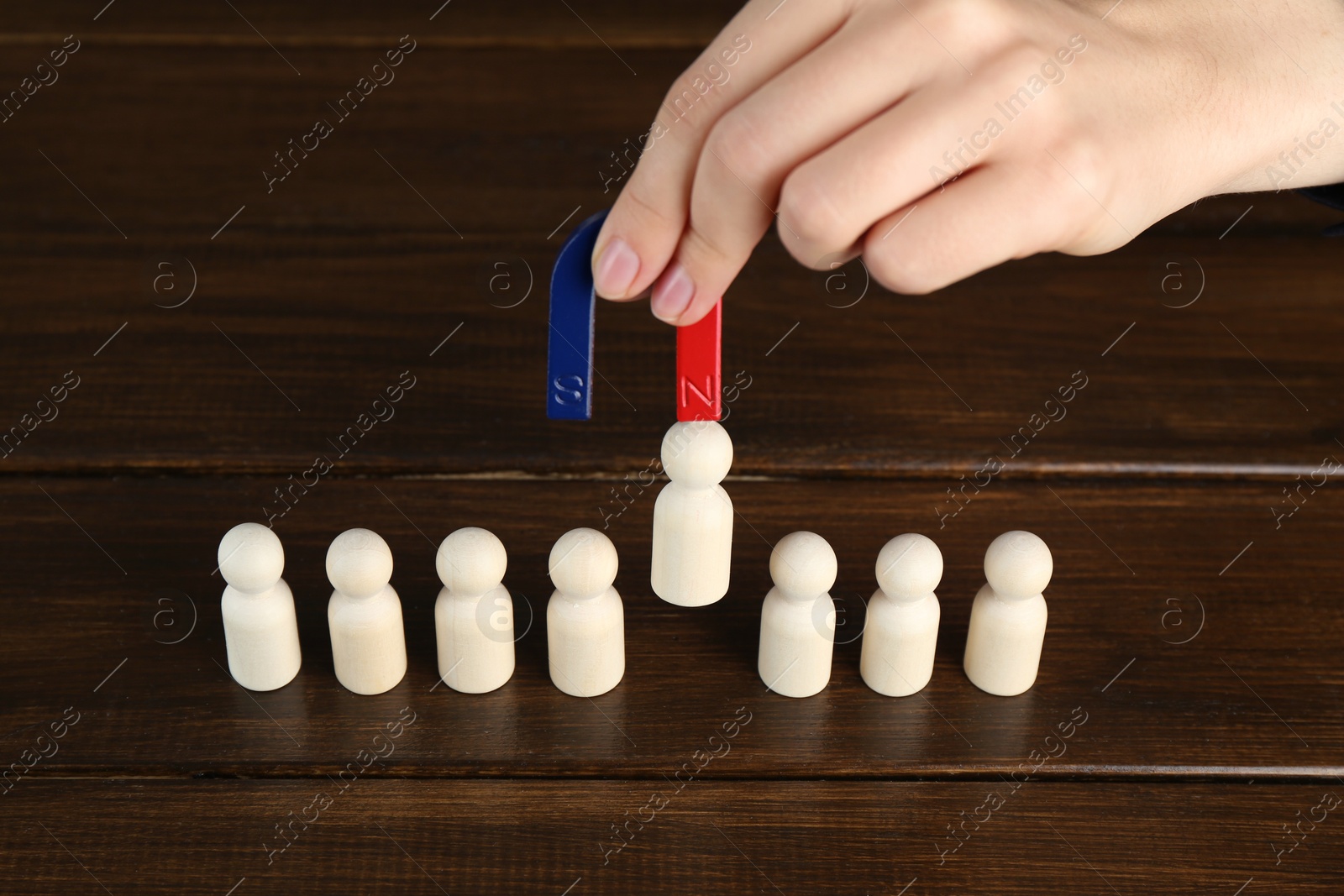 Photo of Woman with magnet attracting piece among wooden ones at table, closeup