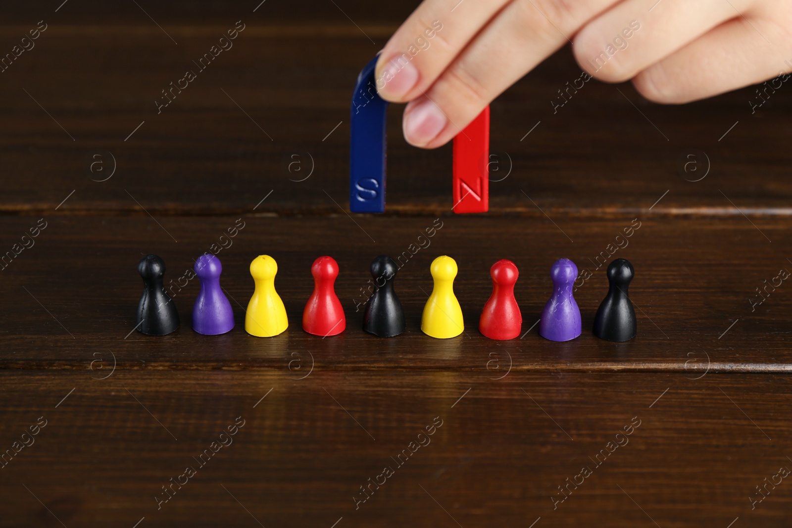 Photo of Woman with magnet attracting different game pieces at wooden table, closeup