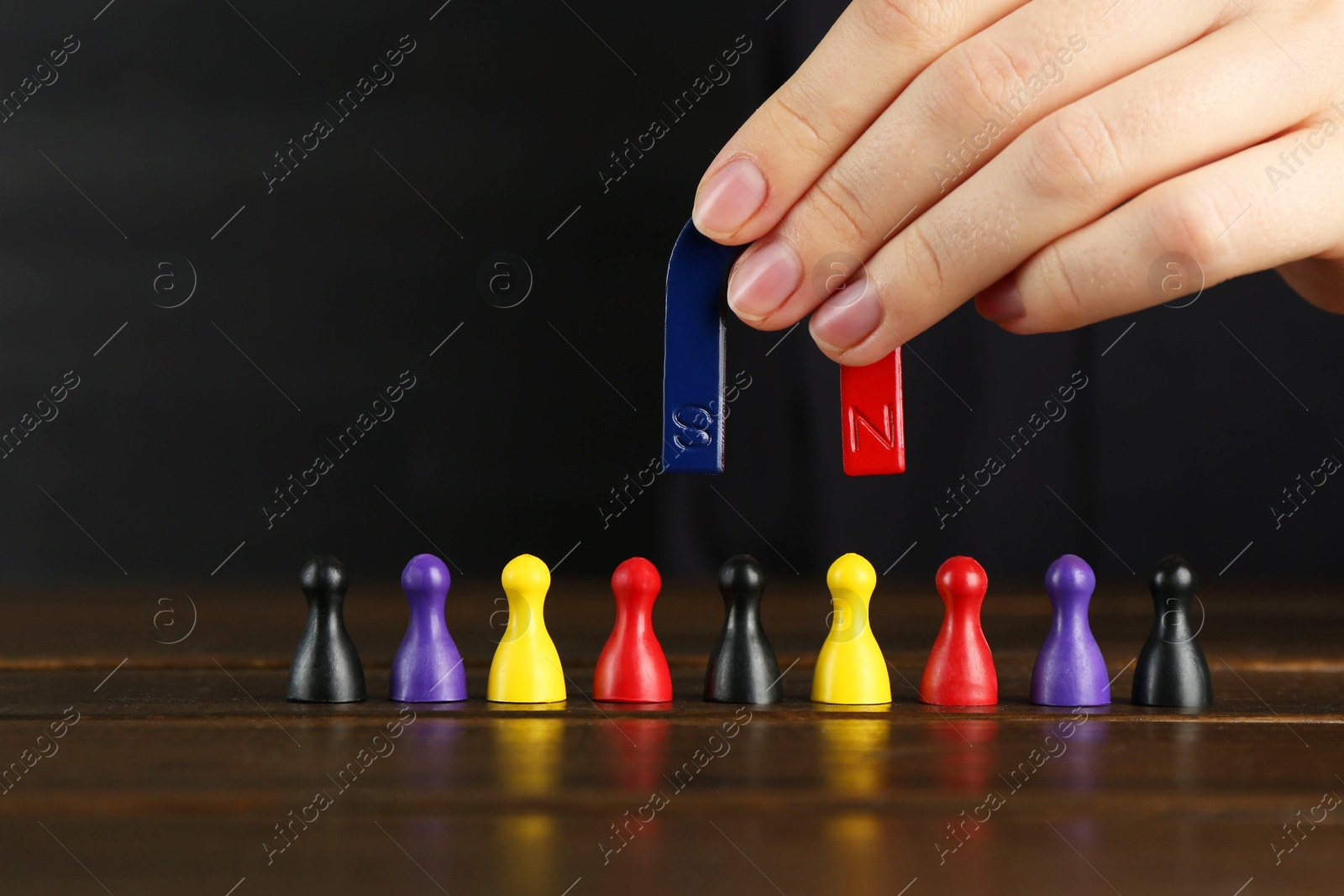 Photo of Woman with magnet attracting different game pieces at wooden table, closeup