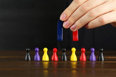 Photo of Woman with magnet attracting different game pieces at wooden table, closeup