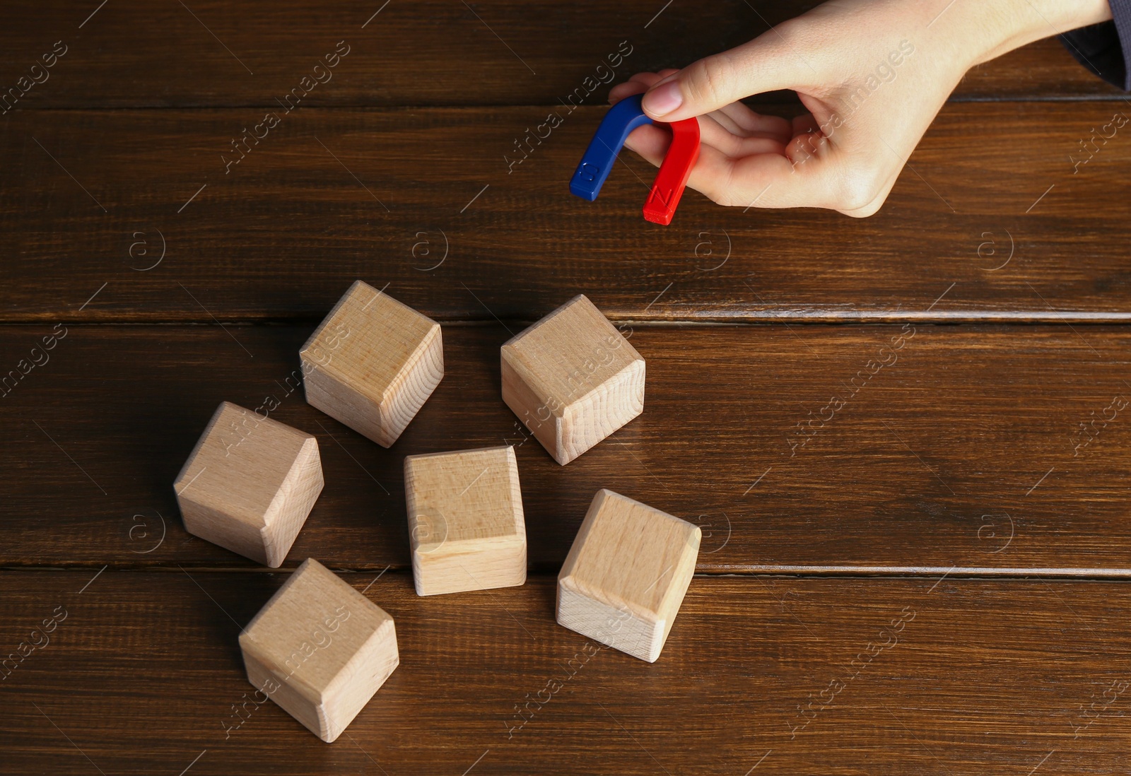 Photo of Woman with magnet attracting cubes at wooden table, closeup