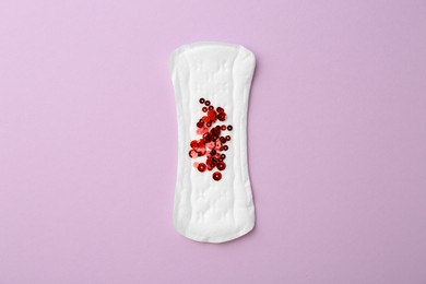 Photo of Menstrual pad with sequins on lilac background, top view