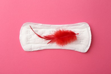 Photo of Menstrual pad with red feather on pink background, top view