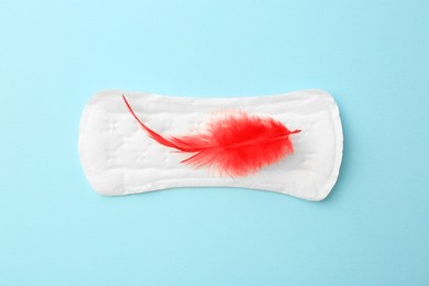 Photo of Menstrual pad with red feather on light blue background, top view