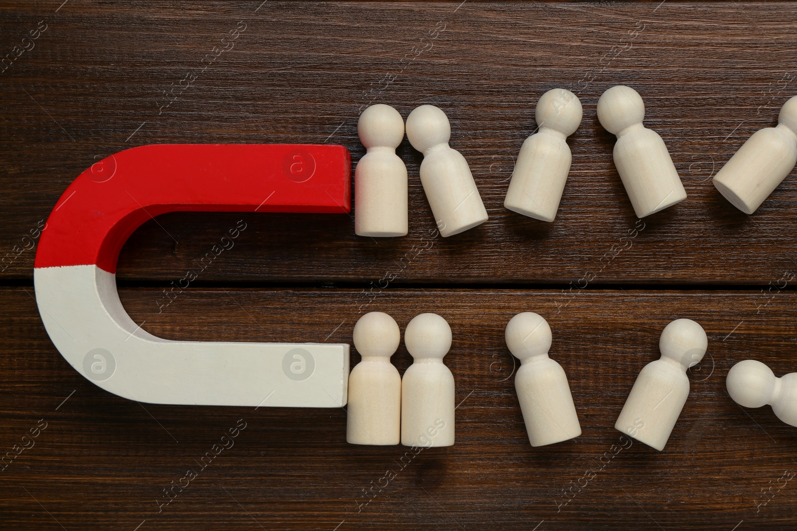 Photo of Magnet attracting human figures on wooden table, flat lay