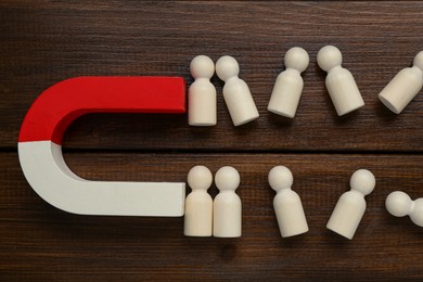 Photo of Magnet attracting human figures on wooden table, flat lay