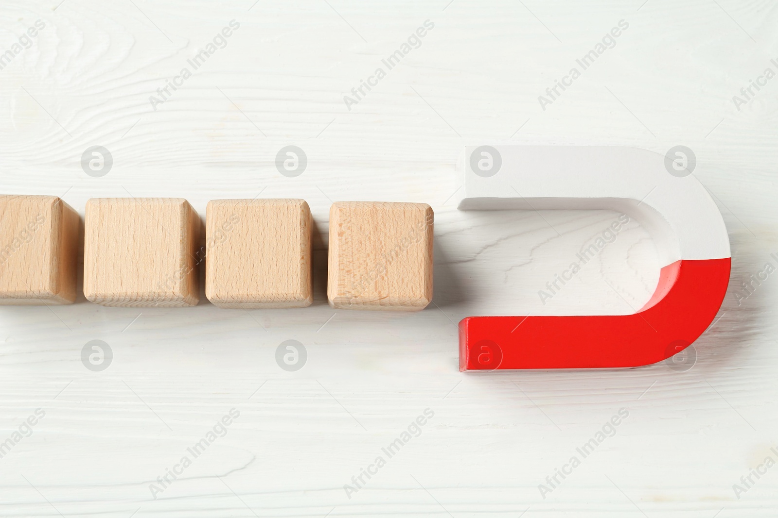 Photo of Magnet attracting cubes on white wooden table, flat lay