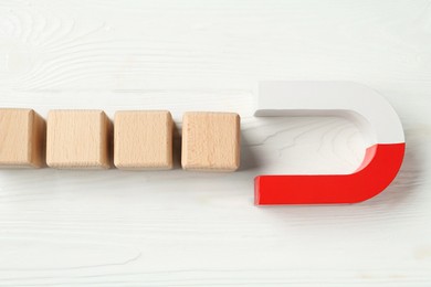 Photo of Magnet attracting cubes on white wooden table, flat lay