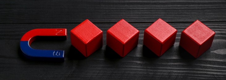 Photo of Magnet attracting red cubes on black wooden table