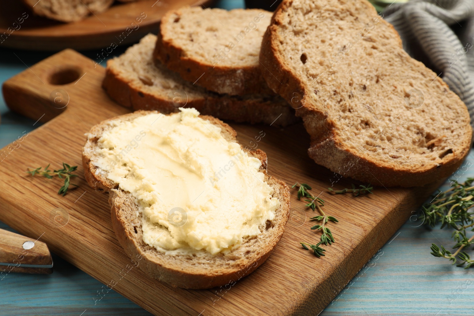 Photo of Fresh bread with butter and thyme on blue wooden table, closeup